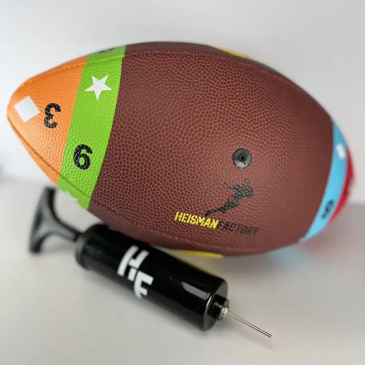 Football with colorful band and 'Heisman Factory' branding, accompanied by a black tool on a white background.