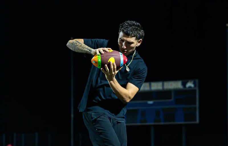 Football player using a ColorTech training football to improve catching and hand-eye coordination under stadium lights.