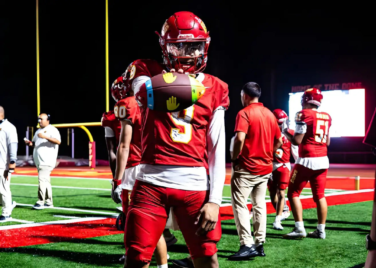 Football player in red uniform holding a ColorTech training football during a nighttime game on the field.